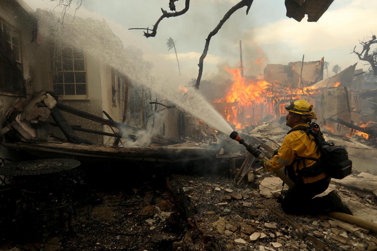 A firefighter aiming a hose at a burning home
